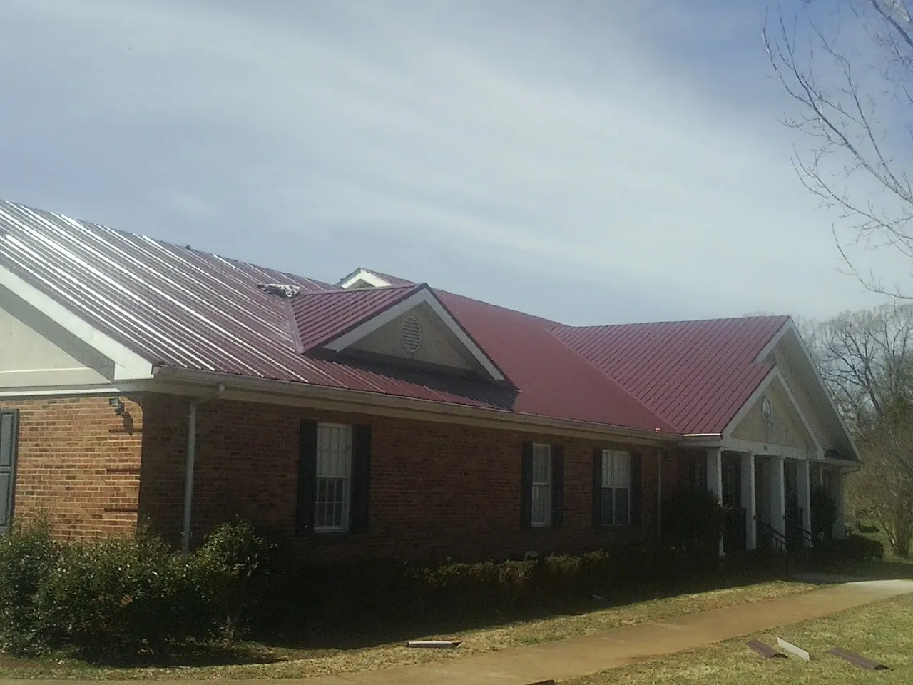Red metal roof with gabled entries on a long brick building, from a Hail Damage Roof Repair job in Watson