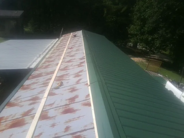 Old rusted panels beside newly installed green metal roofing — Wind Damage Roof Repair by Roofing Brothers in Watson