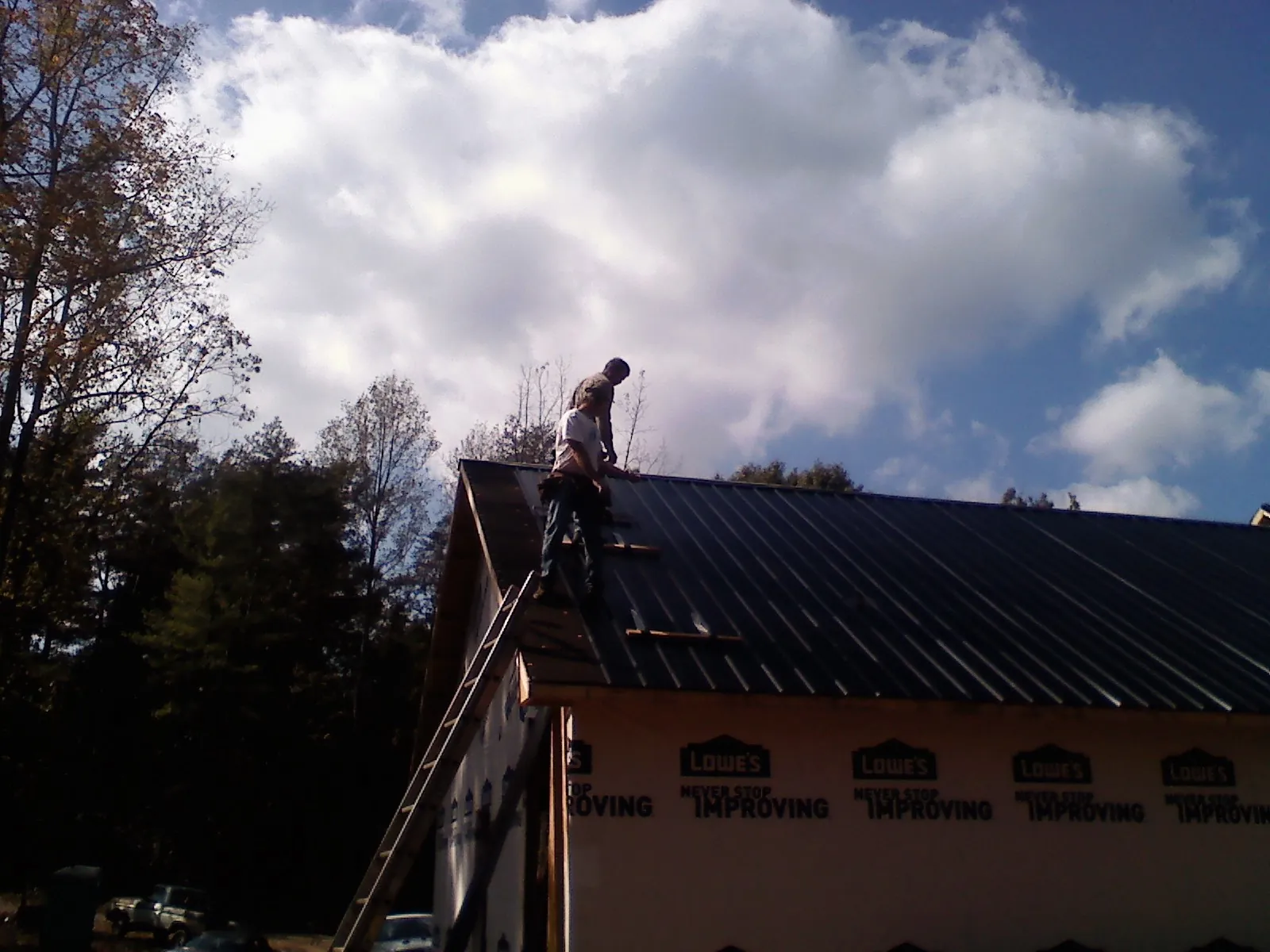 Roofer fastening dark metal panels high against a cloudy sky, from a Roof Inspection job in Watson
